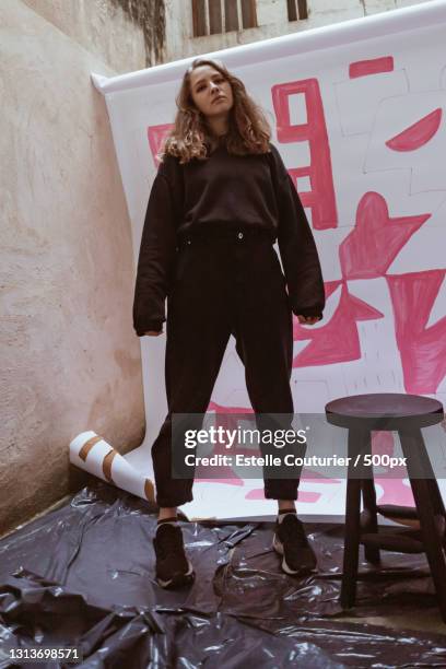 behind the scenes portrait of stylish young woman standing against painting backdrop - photoshoot bts stock pictures, royalty-free photos & images