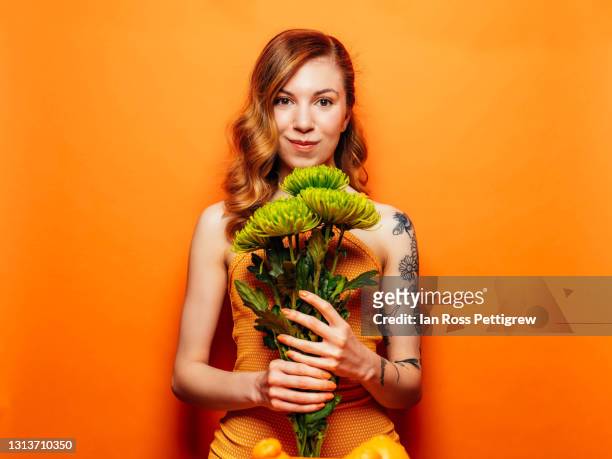 young woman holding green flowers on orange background - portrait orange background stock pictures, royalty-free photos & images