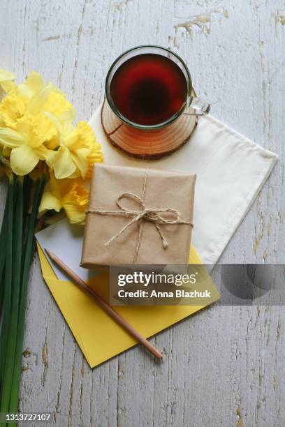 bunch of spring yellow daffodil flowers, cup of coffee, gift box wrapped with brown craft paper, envelope and pencil over gray rustic background. greeting card for spring holidays, mother's day. - pencil skirt beautiful bildbanksfoton och bilder