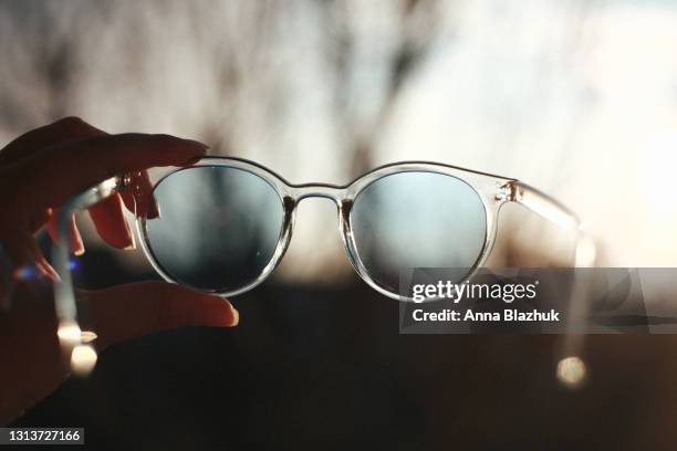 female hand holding blue sunglasses against evening sky, close-up - sunglasses ストックフォトと画像