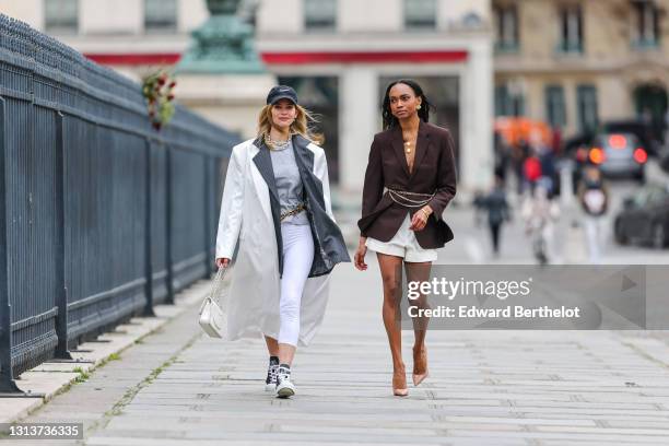 Natalia Verza @mascarada.paris wears a Nike cap hat, a gray striped oversized blazer jacket, a metallic chain necklace, a gray t-shirt, a white long...