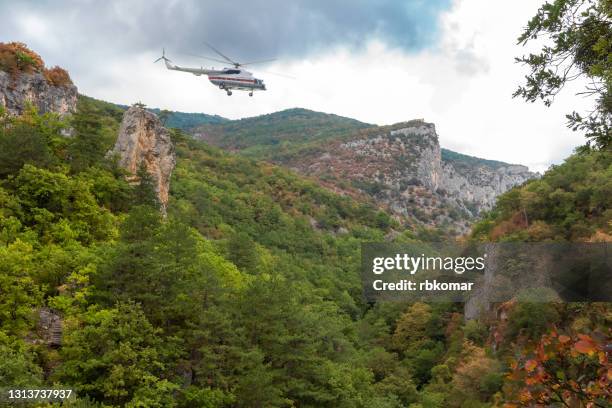 flight of a rescue helicopter hovering in the clouds over a mountain gorge and forest area in cloudy rainy weather. air adventure and travel - helicopter flying over jungle stock pictures, royalty-free photos & images