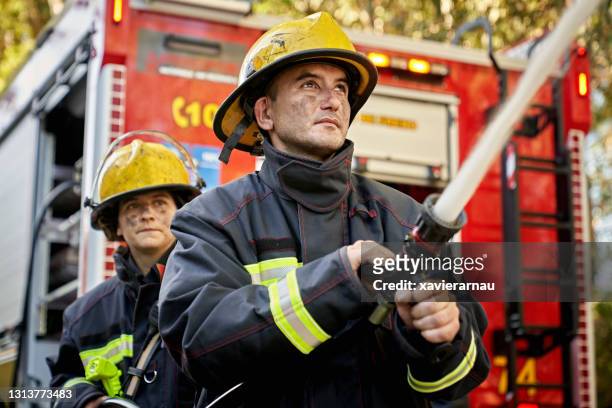 action portrait of male and female firefighting hose team - fire fighting stock pictures, royalty-free photos & images
