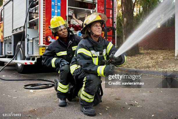 mid adult female hose team che lavora al sito di emergenza - firefighter foto e immagini stock