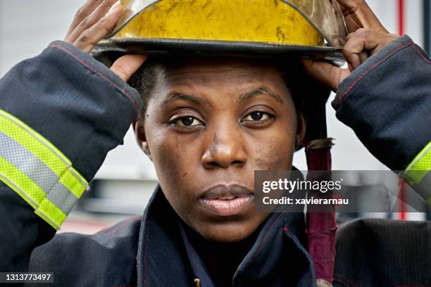 retrato de la mujer negra bombero poniéndose casco - servicios de urgencias y rescate fotografías e imágenes de stock