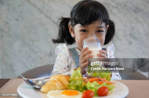 asian little child girl is drinking a glass of milk and enjoy eating a breakfast in the morning - toddler milk stock-fotos und bilder