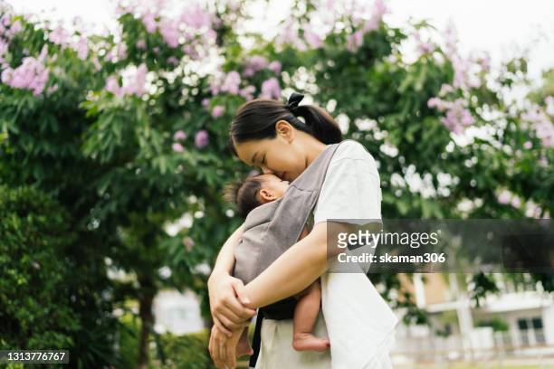 wide angle asian young adult mother embracing  daughter with baby carrier leisure around the garden - asian woman pregnant stock pictures, royalty-free photos & images