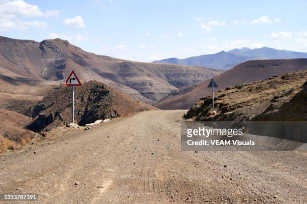 warning dangerous curves sign on a dirt road between high mountains in lesotho. - entre deux photos et images de collection