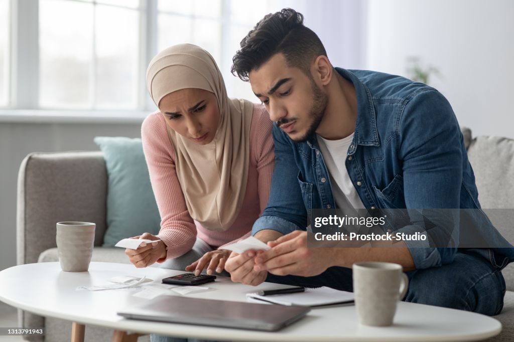 Confusded lady in hijab and her upset husband with bills