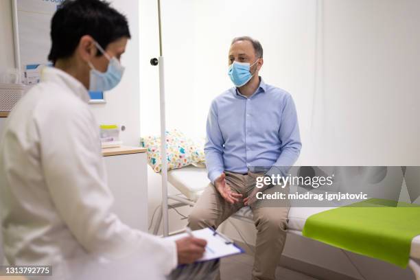 female doctor and patient with protective face masks during medical exam in doctor's office - mask man stock pictures, royalty-free photos & images