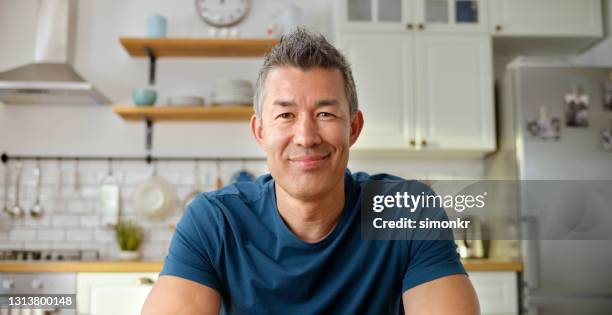 mature man having a video call in kitchen - blue tshirt stock pictures, royalty-free photos & images