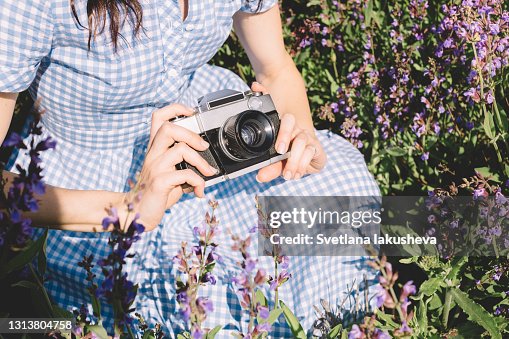 Camera in the hands of a white woman in a blue dress on a background of lavender flowers outdoors Camera in the hands of a white woman in a blue dress on a background of lavender flowers outdoors