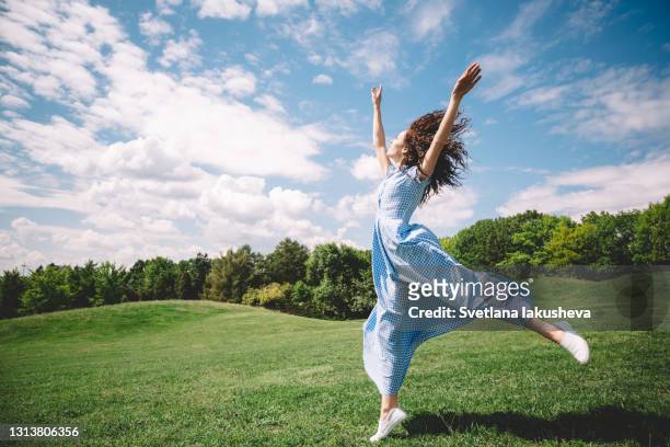 happy young brunette woman jumping high on a summer green meadow in a botanical garden - running shoes sky ストックフォトと画像