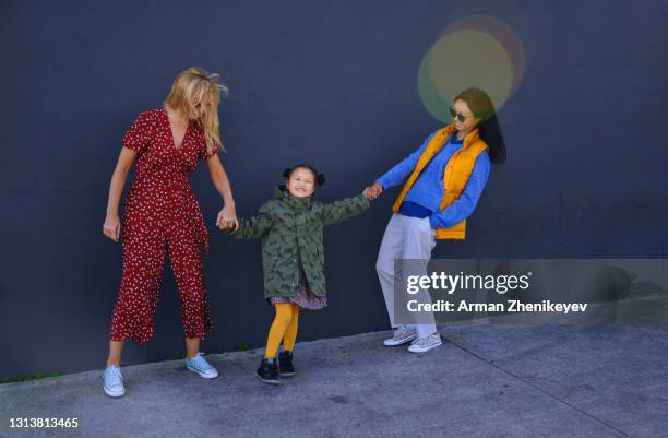 two fashionable women having fun with their daughter next to the wall - fashionable mom stock pictures, royalty-free photos & images