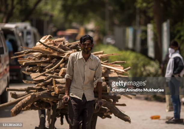 Cemetery worker pulls a cart full of wood logs to be used in a funeral pyre to perform the last rites of the patients who died of the Covid-19...