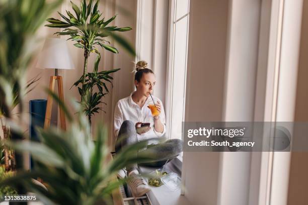 de zitting van de vrouw dichtbij venster en het eten van verse salade en het drinken van sap - windowframe stockfoto's en -beelden