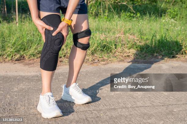 runner woman holding her knee while she having suffering from knee pain and she wearing knee braces for supports to be worn when you have pain in your knee. - knee length stock pictures, royalty-free photos & images