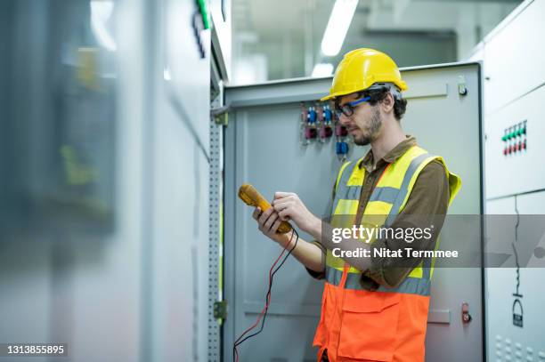 industrial service electrician engineer testing voltage with digital multimeter at a control panel fuse cabinet  in electricity control room of factory. - ampèremètre photos et images de collection