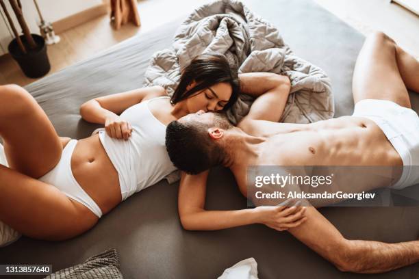 couple engaged in kissing and romantic activity while still wearing underwear in bed - sensualidade imagens e fotografias de stock
