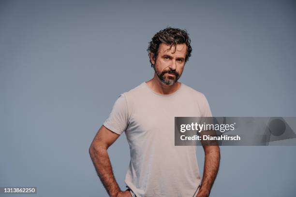 scatto in studio di un uomo maturo serio e bello che indossa semplici abiti casual con capelli naturali neri e grigi guardando la macchina fotografica e avendo le braccia sui fianchi - solo un uomo maturo foto e immagini stock