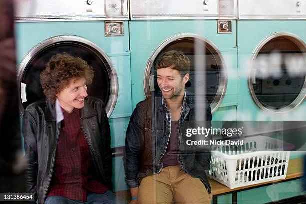 two male friends hanging out doing their washing in a local launderette - launderette stock-fotos und bilder