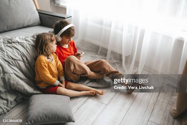 two children boy and girl using mobile phone on sofa at home. - school holiday stock pictures, royalty-free photos & images