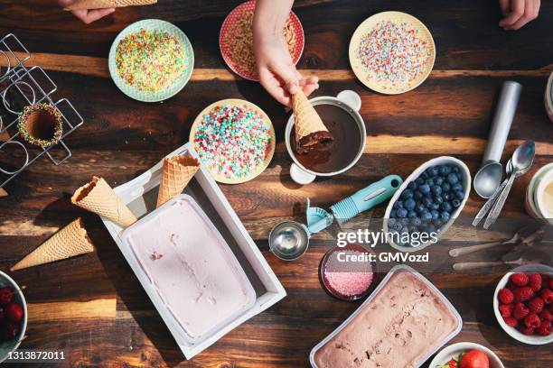 little girls preparing ice cream in cone with various toppings, fruits, and candy sprinklers - ice cream sprinkles stock pictures, royalty-free photos & images