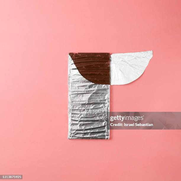 top view of a dark chocolate bar in its half-opened aluminum wrapper on a pink background. - chocolate square stock pictures, royalty-free photos & images