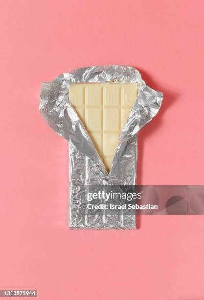 top view of a white chocolate bar in its half-opened aluminum wrapper on a pink background. - candy wrapper stock pictures, royalty-free photos & images
