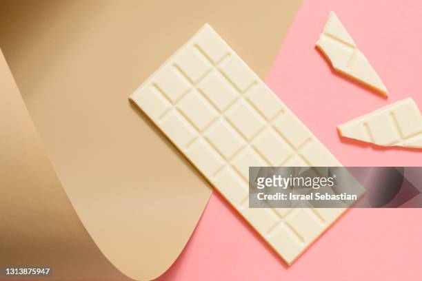 top view of a whole bar of white chocolate along with pieces of the same chocolate on pink and brown background. - chocolate top view imagens e fotografias de stock