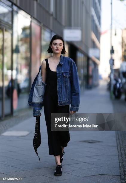 Celine Bethmann wearing black midi dress, blue Levis denim jacket, black bag and black Adidas sneakers on April 20, 2021 in Berlin, Germany.