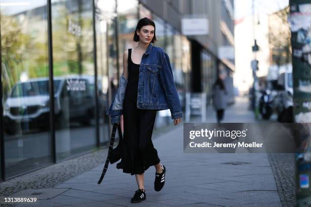 Celine Bethmann wearing black midi dress, blue Levis denim jacket, black bag and black Adidas sneakers on April 20, 2021 in Berlin, Germany.