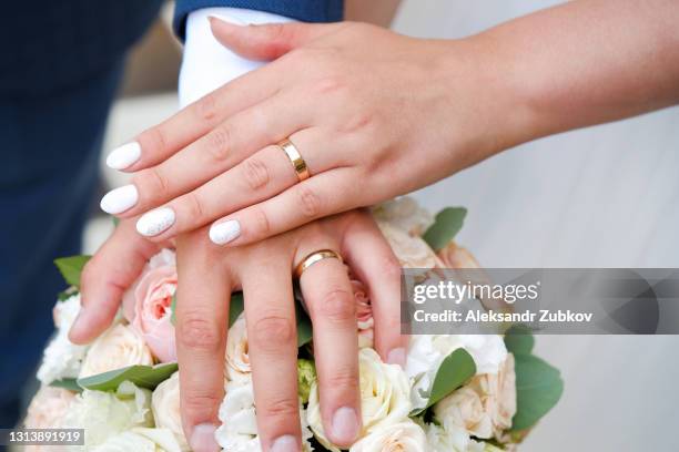 hands of the bride and groom on a wedding bouquet of roses and green leaves. wedding rings on the fingers of the newlyweds. - finger ring stock pictures, royalty-free photos & images