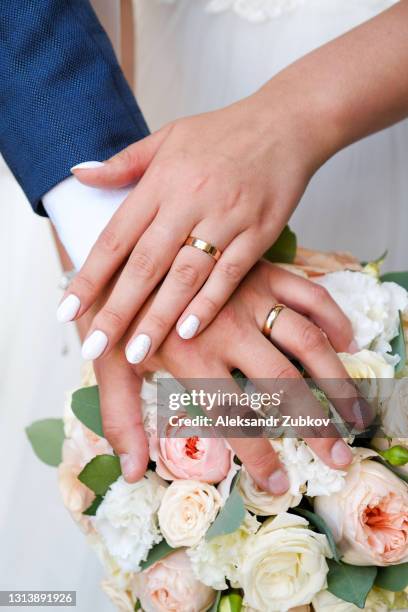 hands of the bride and groom on a wedding bouquet of roses and green leaves. wedding rings on the fingers of the newlyweds. - cerimônia de casamento imagens e fotografias de stock