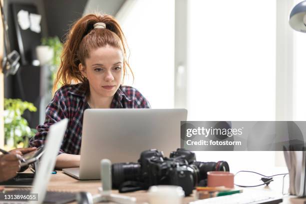 young female graphic designer sitting at her desk and working on laptop - graphic design studio stock pictures, royalty-free photos & images