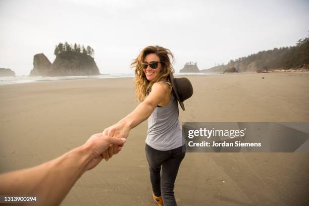 a woman running on a beach holding a mans hand. - escapismo foto e immagini stock