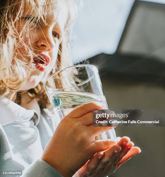 young girl holds a glass of water - niño-tomando-agua fotografías e imágenes de stock