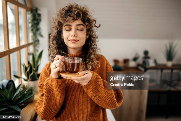 ritratto di giovane bella donna che beva un tè nel suo appartamento - capelli ricci foto e immagini stock