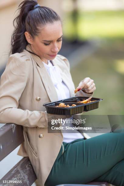 woman in business clothes eats chicken nuggets and chips from a portable plastic container sitting on a bench on the street. - eating chicken nuggets stock pictures, royalty-free photos & images