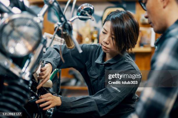 medio volwassen vrouwelijke monteur die een motorfiets aan een cliënt toont - bike mechanic stockfoto's en -beelden