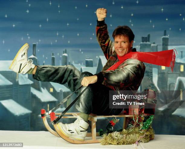 Singer Cliff Richard posed on a sledge in a snowy Christmas scene, circa December 1990.