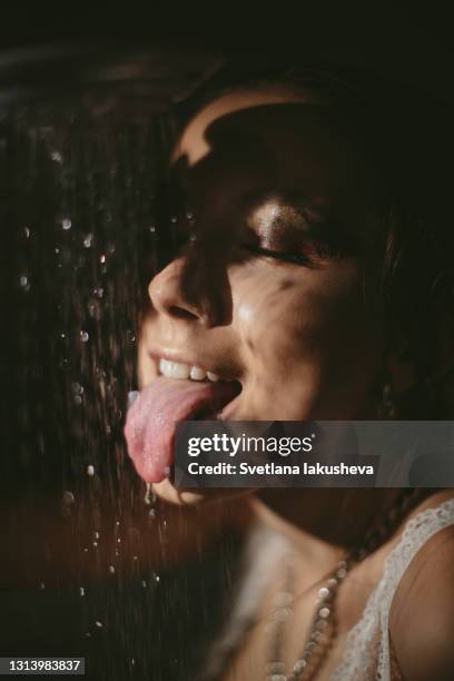 portrait of young brunette woman in low key in lingerie through water stream of drops from shower. the model looks down. - soft focus eye water stock-fotos und bilder