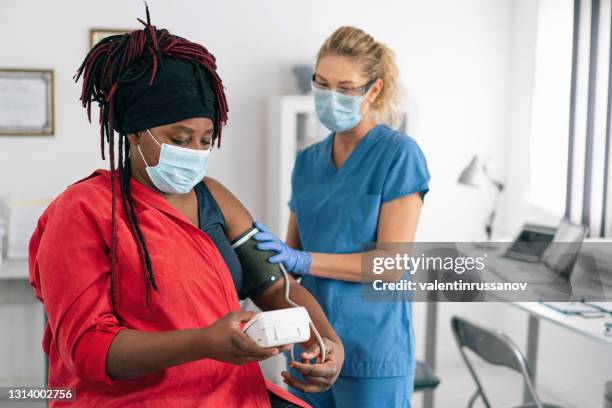 mujer afro que mide su presión arterial durante un chequeo con una enfermera, antes de recibir una vacuna covid-19 - protocolo de bioseguridad fotografías e imágenes de stock