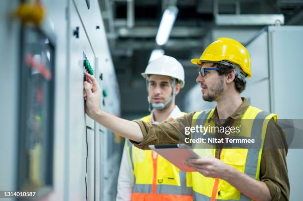 industrial service electrician engineers standing side by side having exchange idea in front of electricity control board. energy management system (ems) concept. - energieeffizienz stock-fotos und bilder