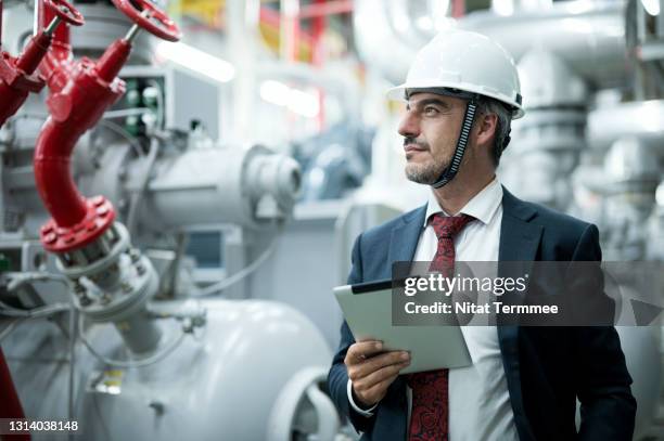 mature businessman with tablet in a factory boiler control room. industrial boiler room ventilation. - international economic assistance stock pictures, royalty-free photos & images