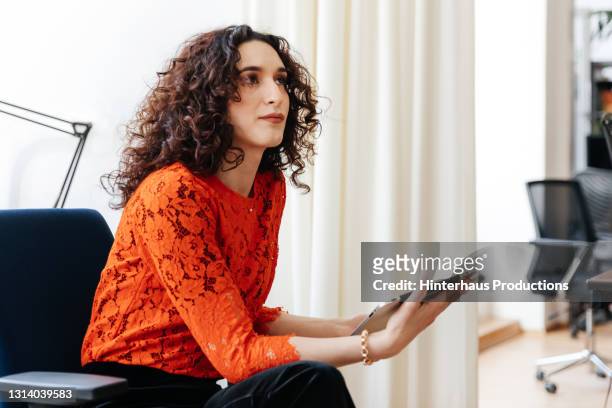 transgender woman listening while holding digital tablet in office - concepts & topics stock pictures, royalty-free photos & images