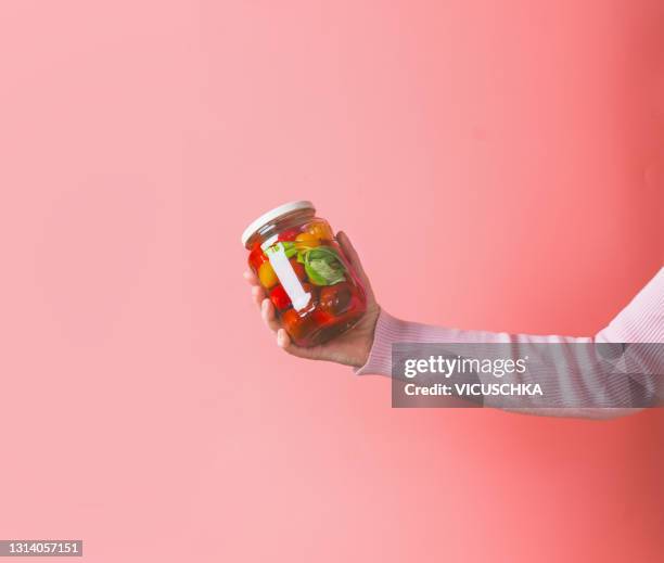 woman hands with light pink sweatshirt holding glass jar with various preserved food on pink background - eingelegt stock-fotos und bilder