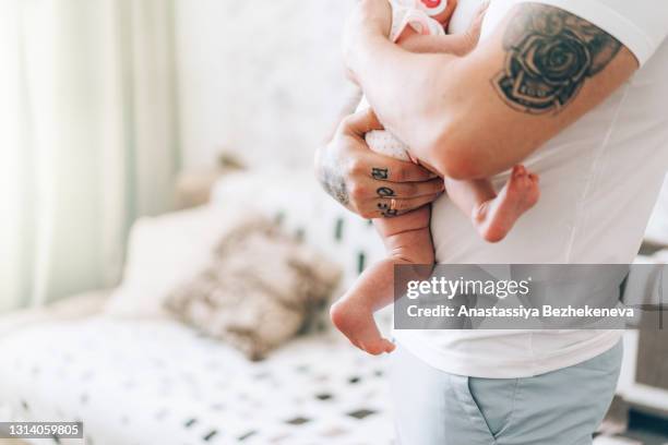 young father with tattoo is holding his newborn baby in his arms and shakes. love and care for children. adoption of children - father in law stockfoto's en -beelden