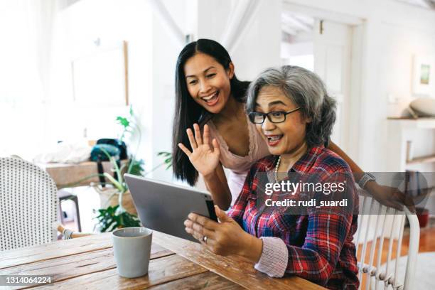 smiling woman and daughter on video call over digital tablet - indonesia family imagens e fotografias de stock