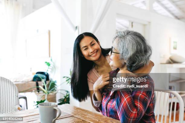 liebevolle erwachsene tochter umarmt fröhliche seniorin zu hause - asian mother daughter stock-fotos und bilder